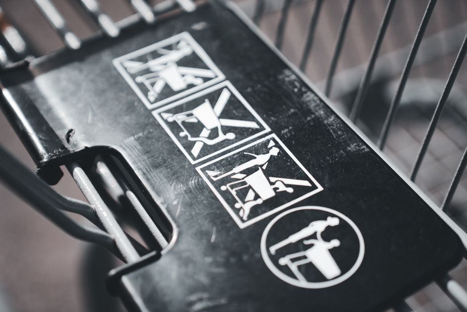 Close-up of white safety pictograms on a black metal shopping cart handle, illustrating use and tipping cautions.