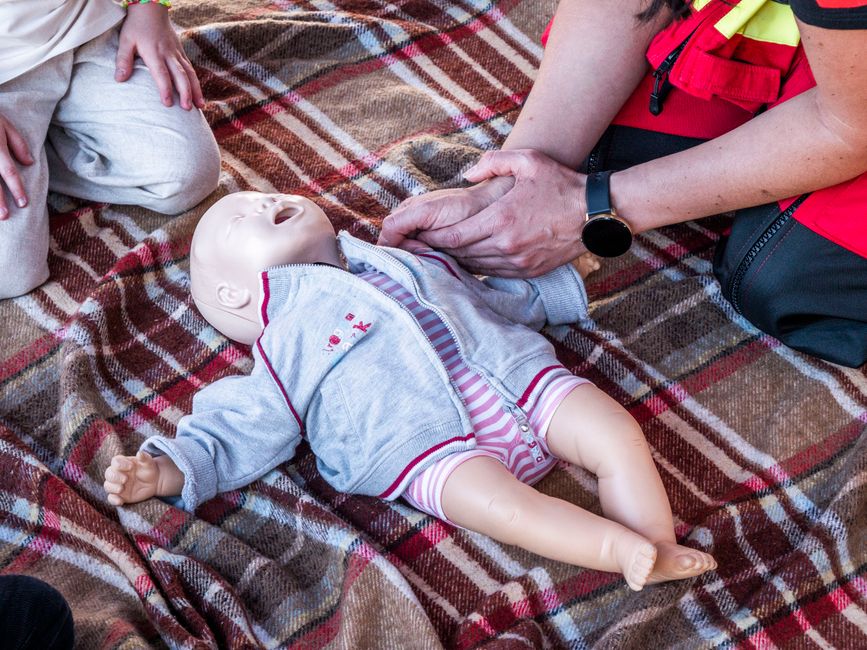Person practicing infant CPR on a baby doll lying on a plaid blanket during first aid training