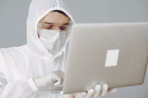 Scientist in full protective gear typing on a laptop in a lab