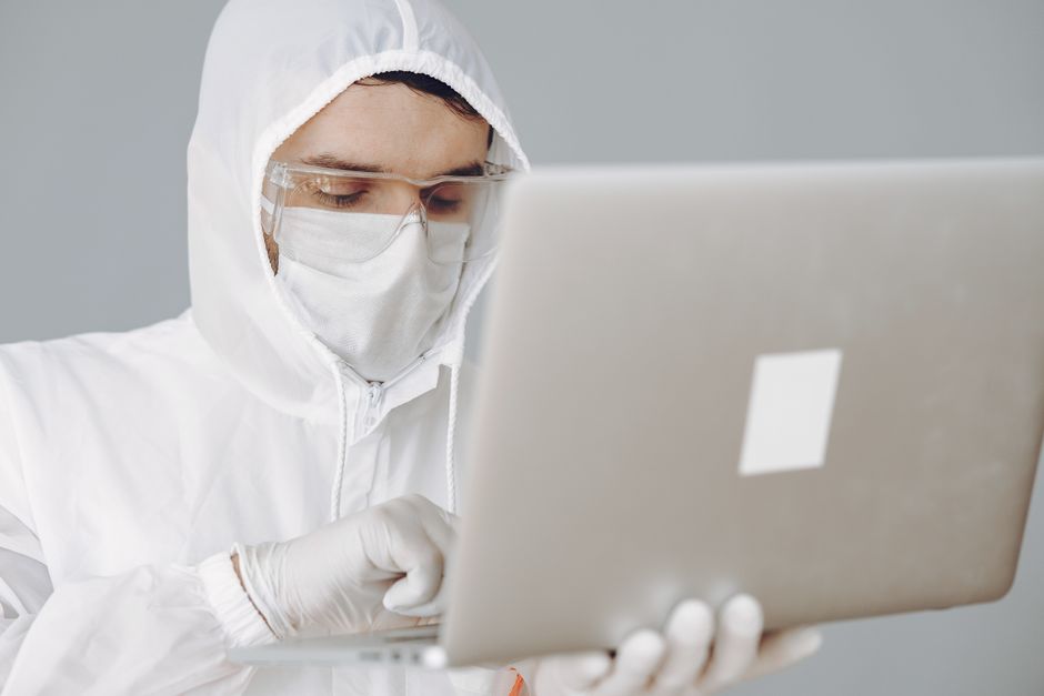 Scientist in full protective gear typing on a laptop in a lab