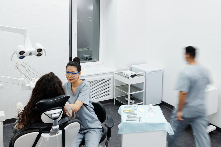 Dentist in scrubs with protective glasses treats a patient in a bright dental clinic.