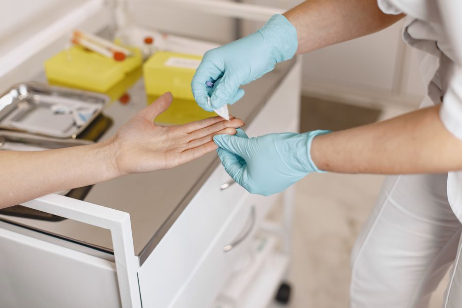 Healthcare worker in blue gloves wipes a patient's finger for a blood test in a clinical setting.
